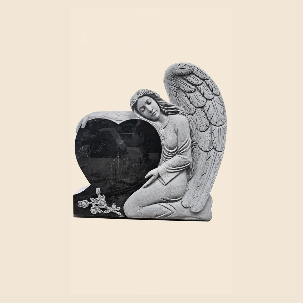 Carved angel beside a black granite heart with roses at the base