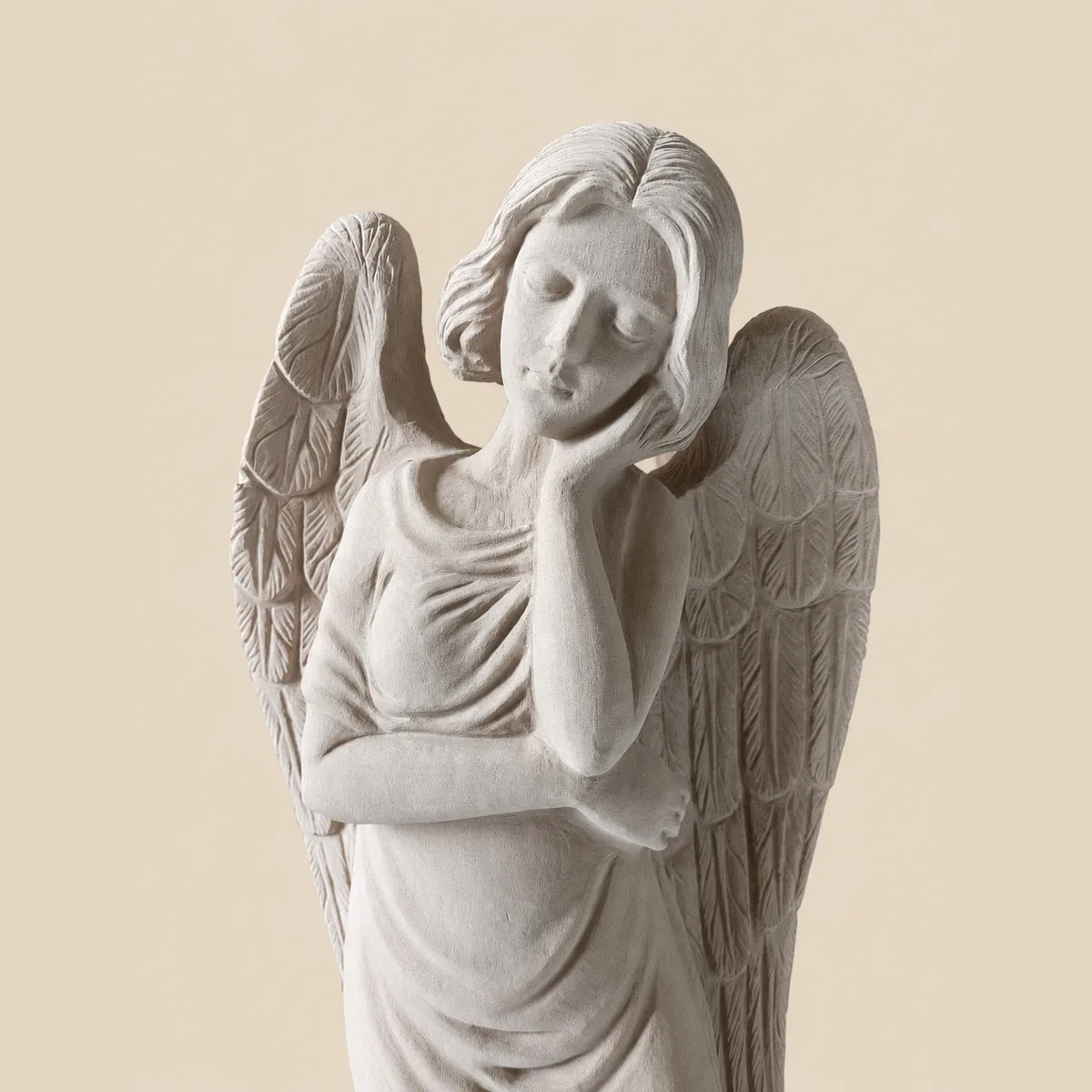 Standing angel with folded wings and a hand to her cheek, in cream granite
