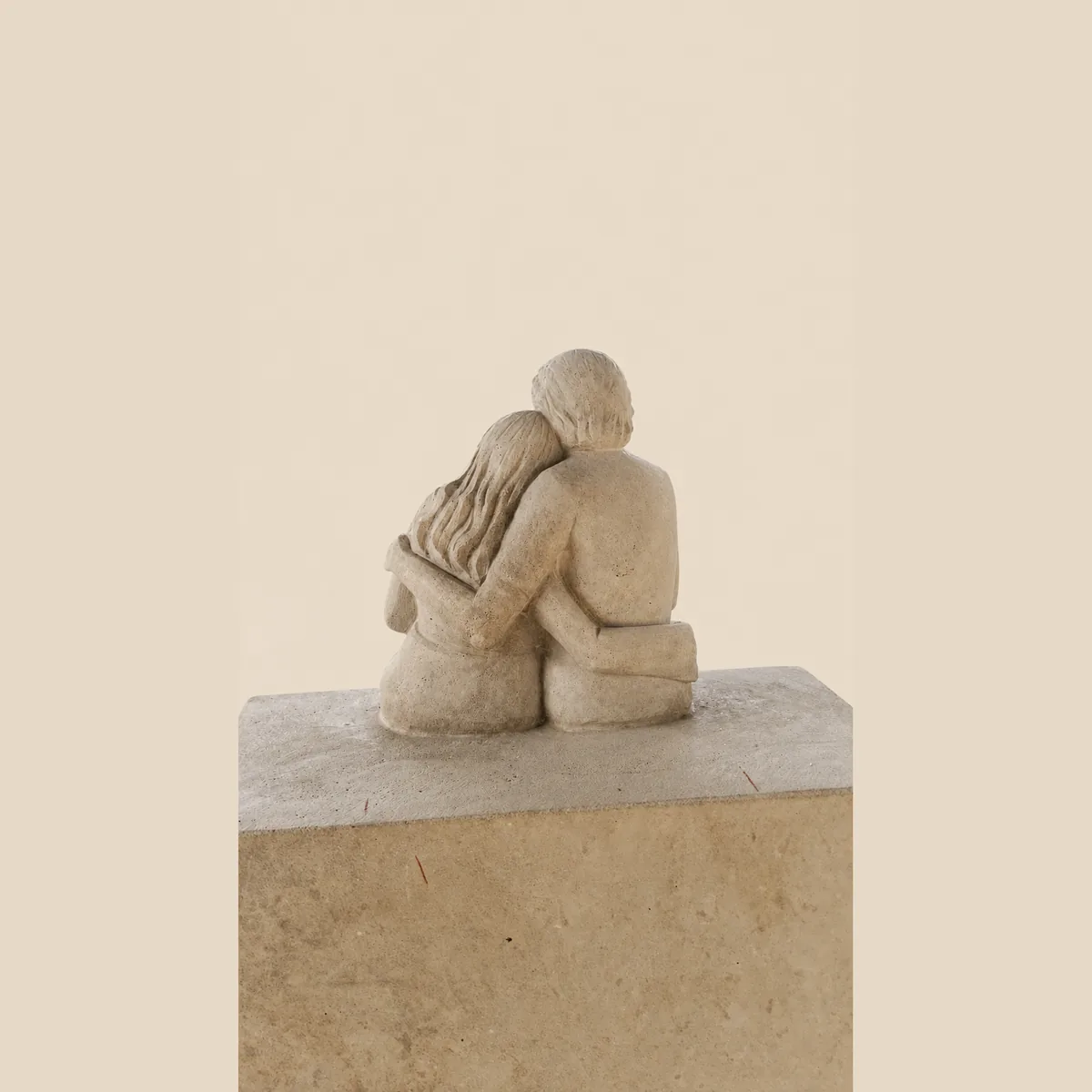 Couple seated arm in arm, carved in cream granite on a plain block