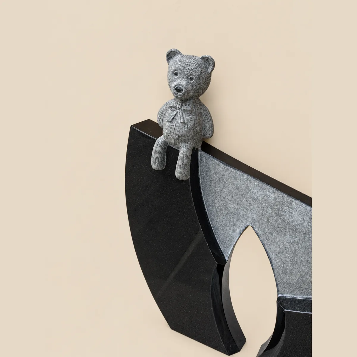 Grey granite teddy bear seated on a polished black arched memorial